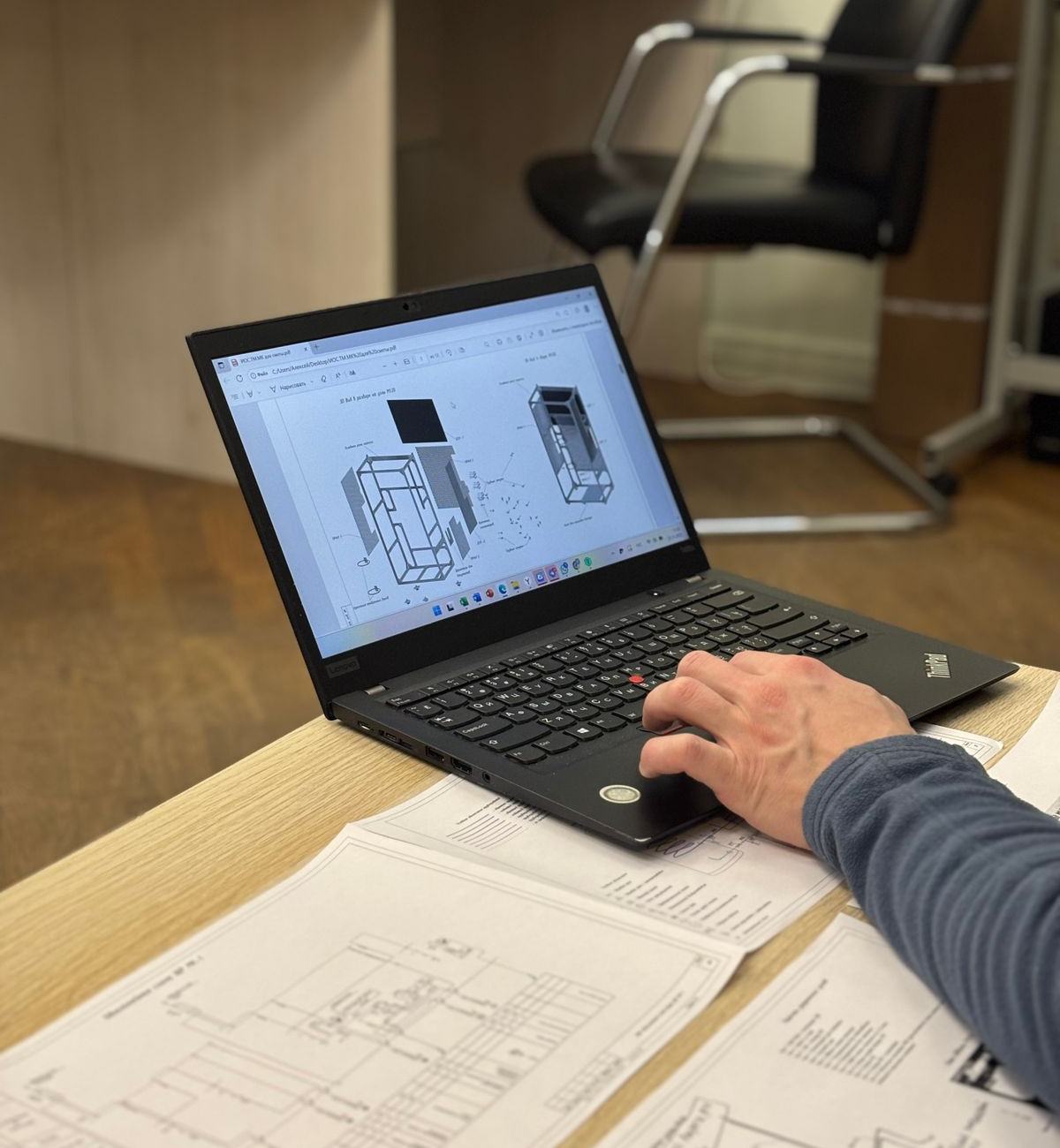 Ingeniero modelando una pieza en 3D junto a planos de taller